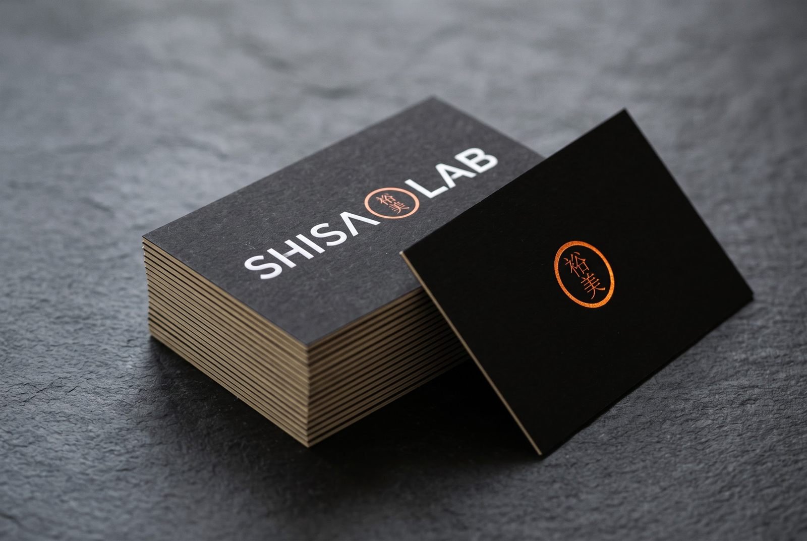 Cartões de visita pretos com o logo Shisa Lab em branco e o anel laranja, sobre pedra escura
