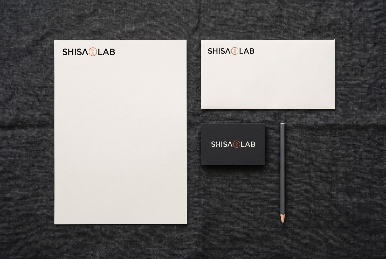 Papel timbrado e envelope marfim com o logo Shisa Lab sobre linho grafite
