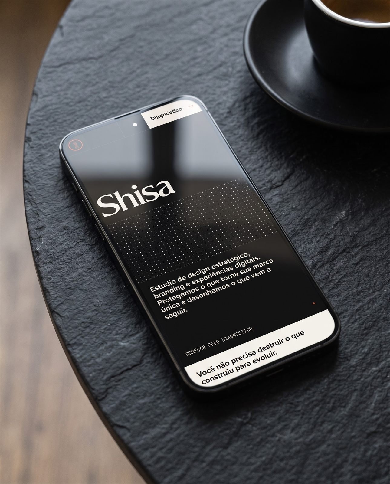 Celular sobre mesa de ardósia exibindo o site da Shisa