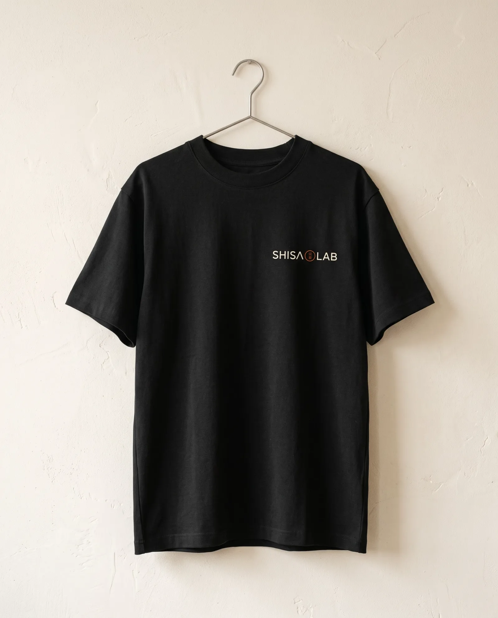 Camiseta preta pendurada com o wordmark Shisa Lab pequeno no peito